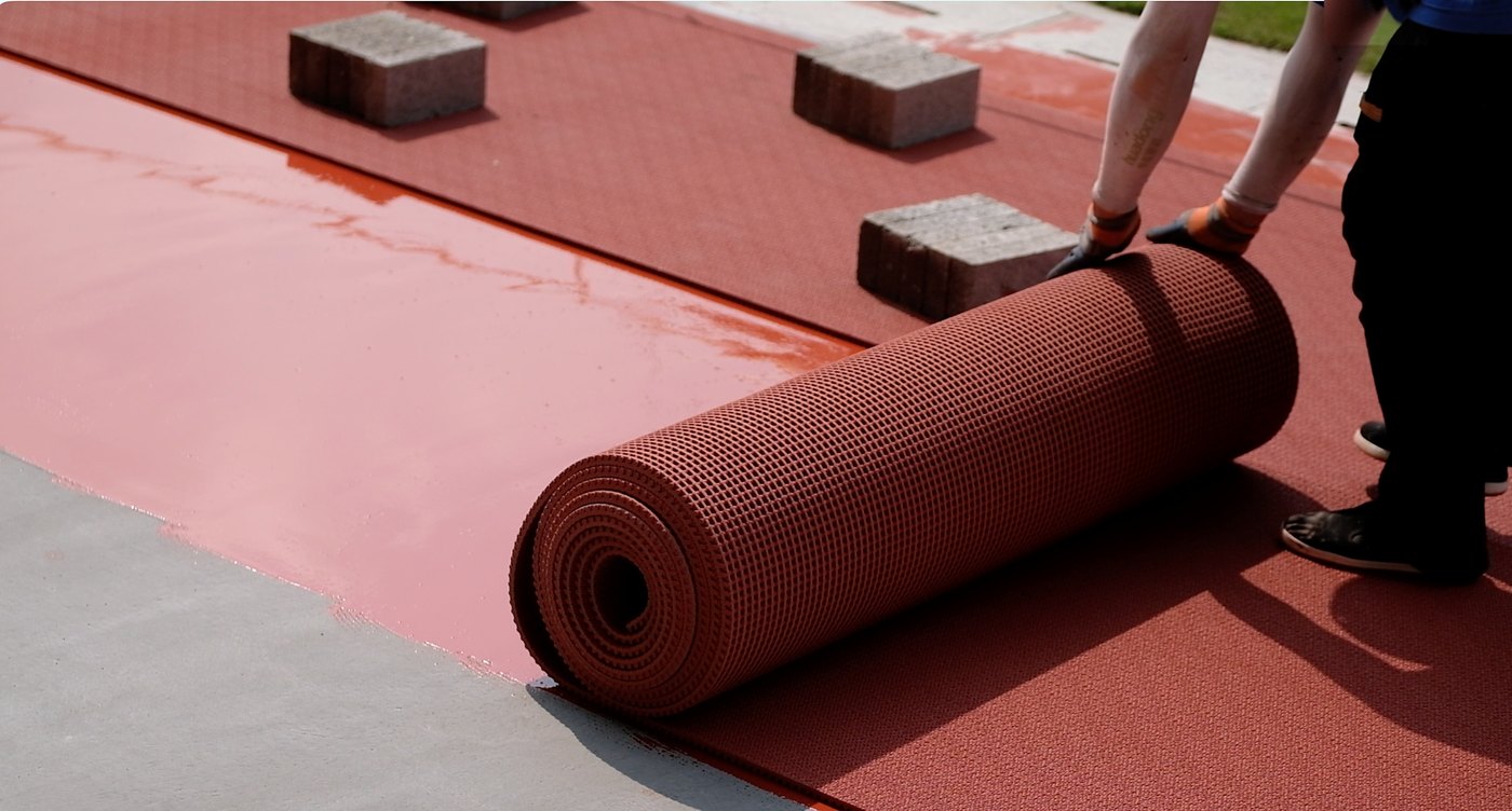 Prefabricated rubber track roll being laid onto an adhesive-covered base